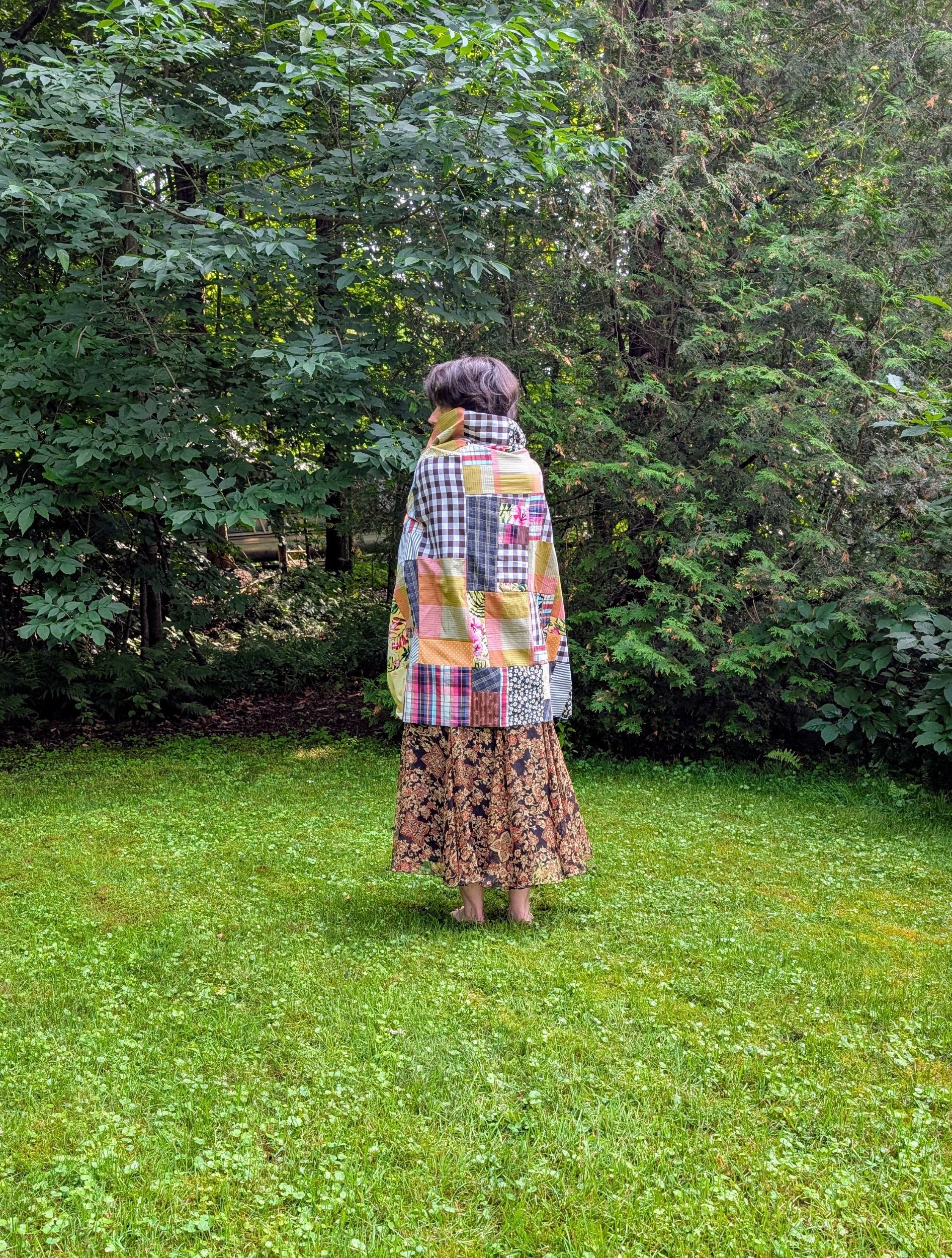 Woman wrapped in a warm, patchwork quilt stands outdoors, radiating comfort and warmth.