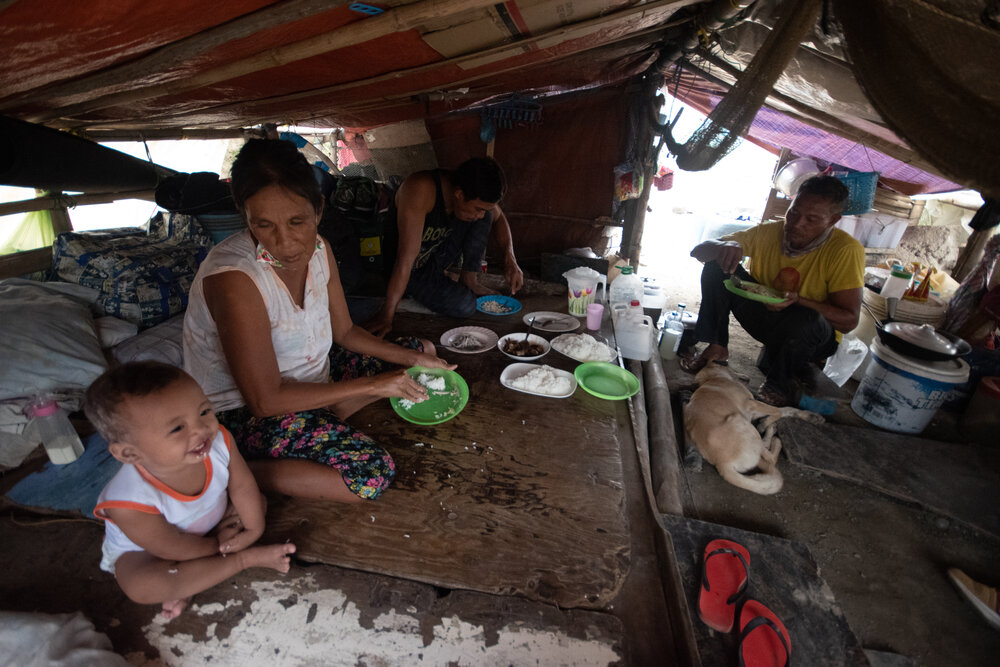  Eduardo and his family eat lunch inside their makeshift tent. In between cooking and preparing for his fishing trip later that day, what worries him is how his four children in Bulacan are coping without their parents. He smiles as he recalls how ha