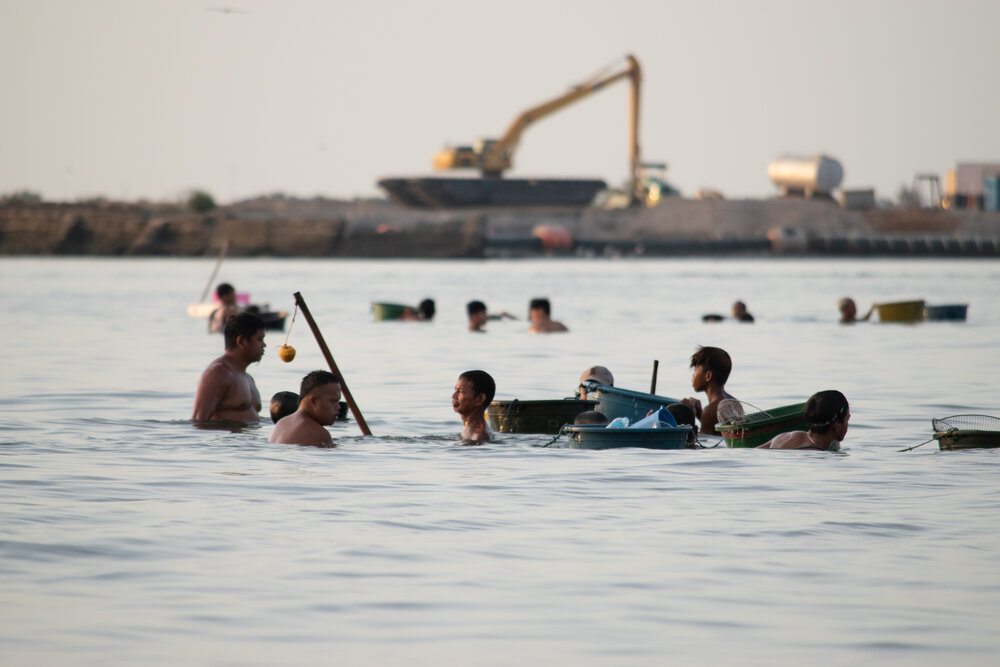  People forage for shellfish as water gets shallow during low tide along the coast of Barangay Tangos South in Navotas City. In the background, a backhoe is parked on a reclamation site. People there have been told they would need to relocate soon to