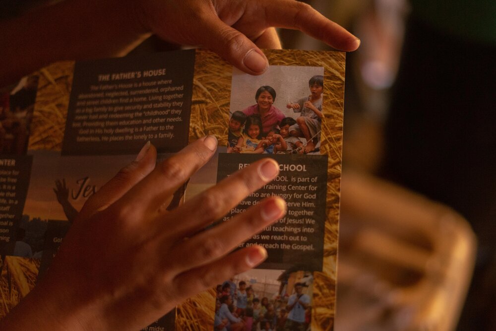  Amy shows a photo of two of her sons on her church's brochure on April 9, 2021. It’s the only picture of her sons that she was able to keep at her Smokey Mountain home. When her pastor visits her, he sets up a video call so she can talk to her sons.
