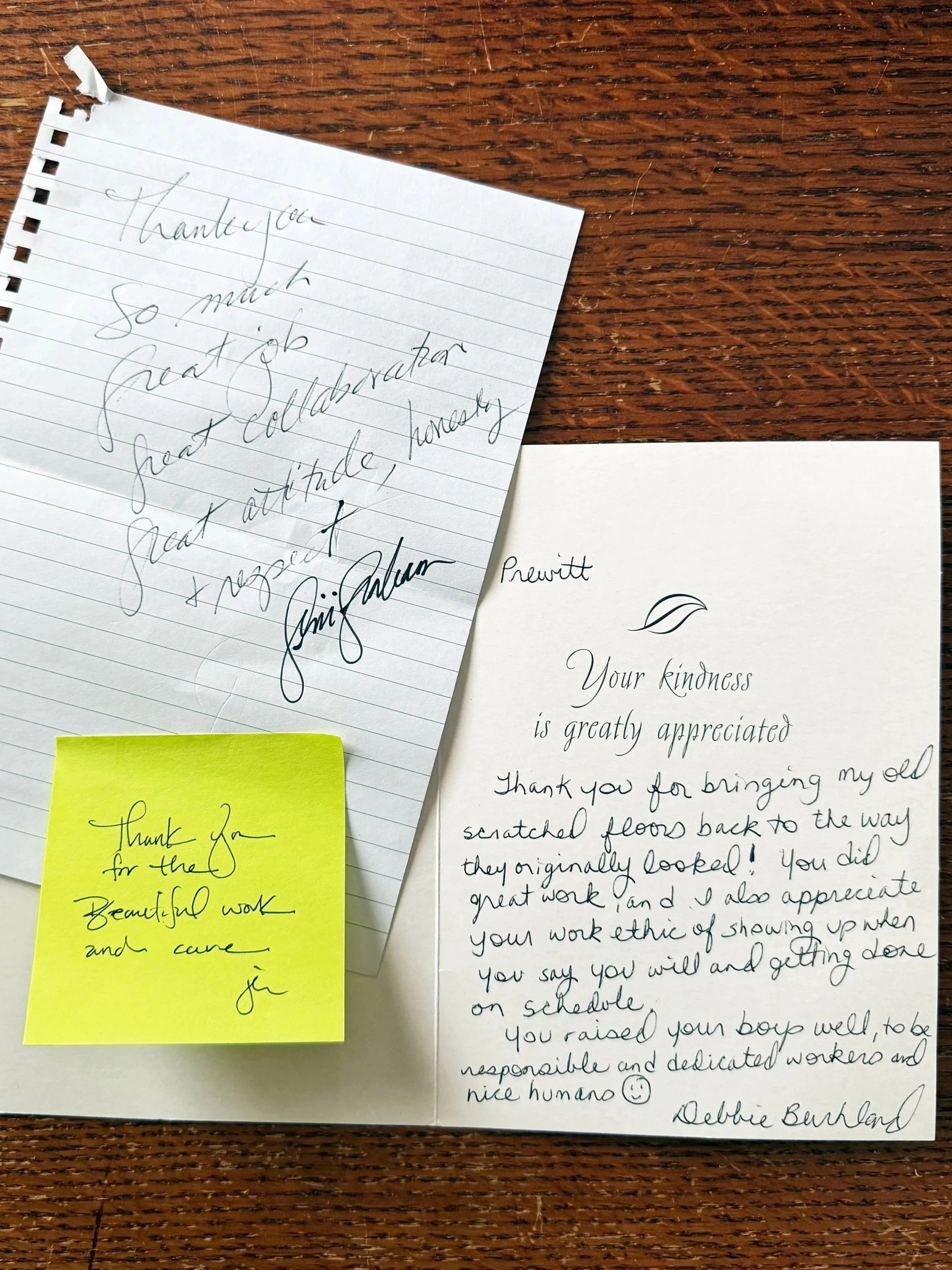 A handwritten thank you note on lined paper, a printed appreciation card with a handwritten message, and a yellow sticky note with a thank you message, all placed on a wooden surface.