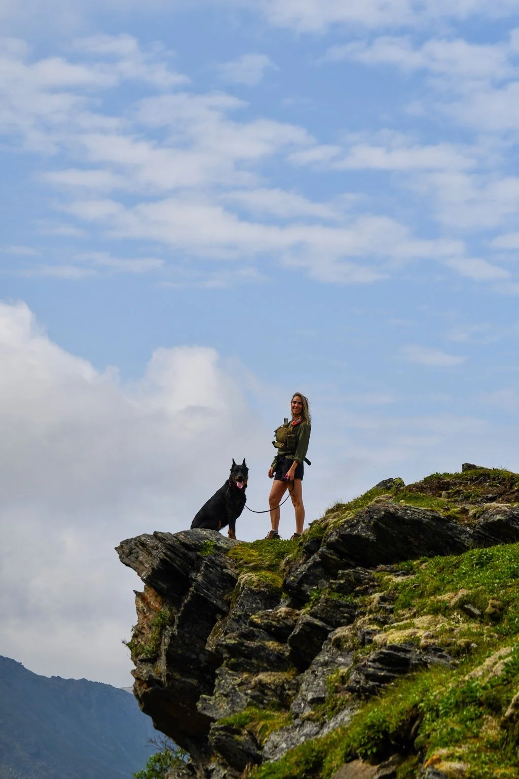 An owner and Beauceron explore a rocky mountain ridge.