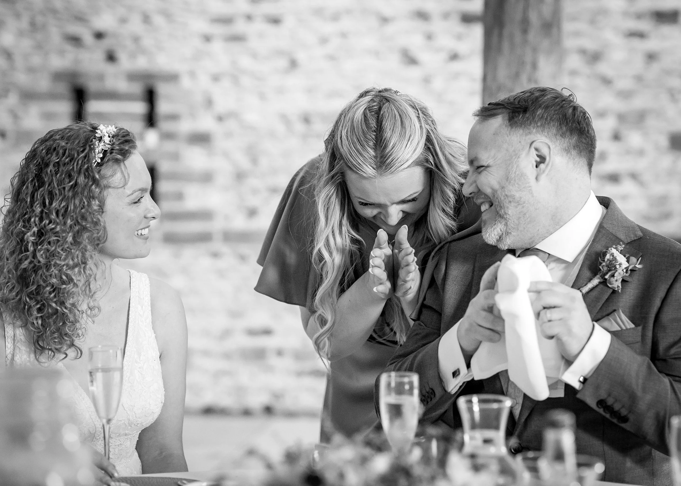 Bride and groom laughing during speeches at Upwaltham Barns in West Sussex, captured in a natural, candid wedding photograph.