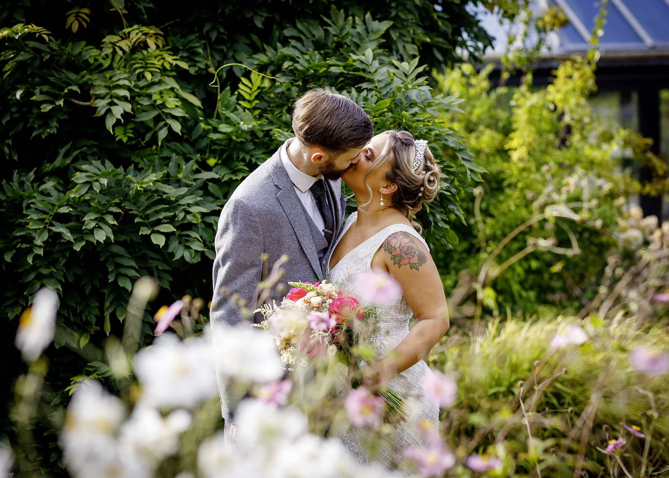Bride and groom kissing in the gardens at Horsham Register Office, captured in a natural, candid wedding photograph surrounded by greenery