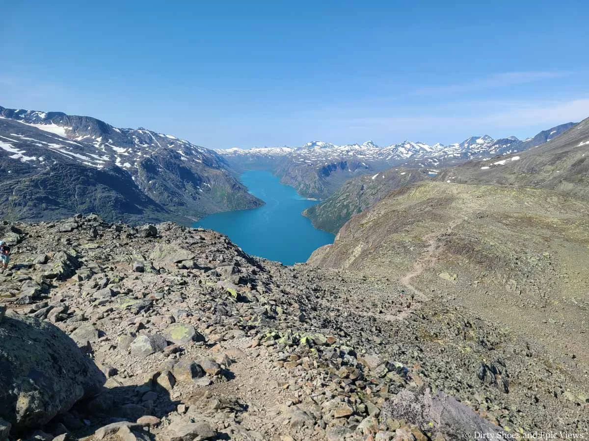 A herd path descends down a rocky mountain plateau with lake and mountain views on the Besseggen Ridge trail in Norway
