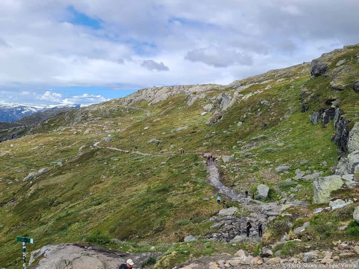 A narrow dirt path crosses a grassy slope on the Trolltunga trail