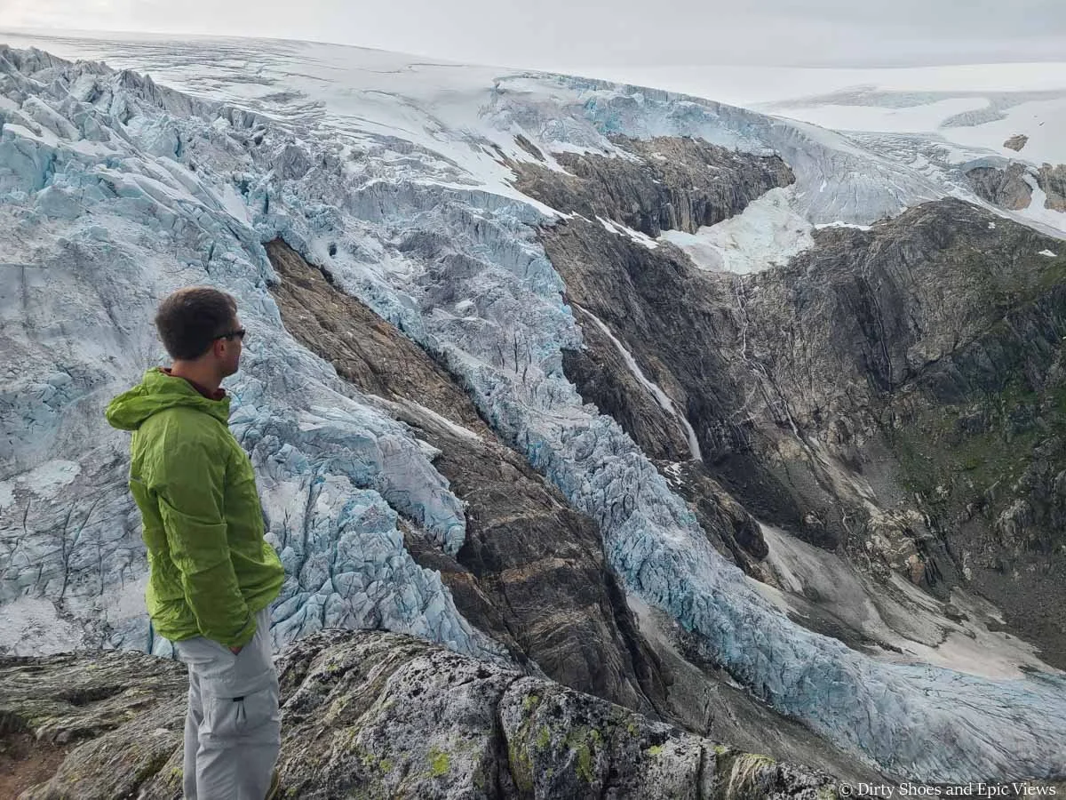 A hiker looks out over a cascading glacier fall into a deep valley from the Reinanuten viewpoint