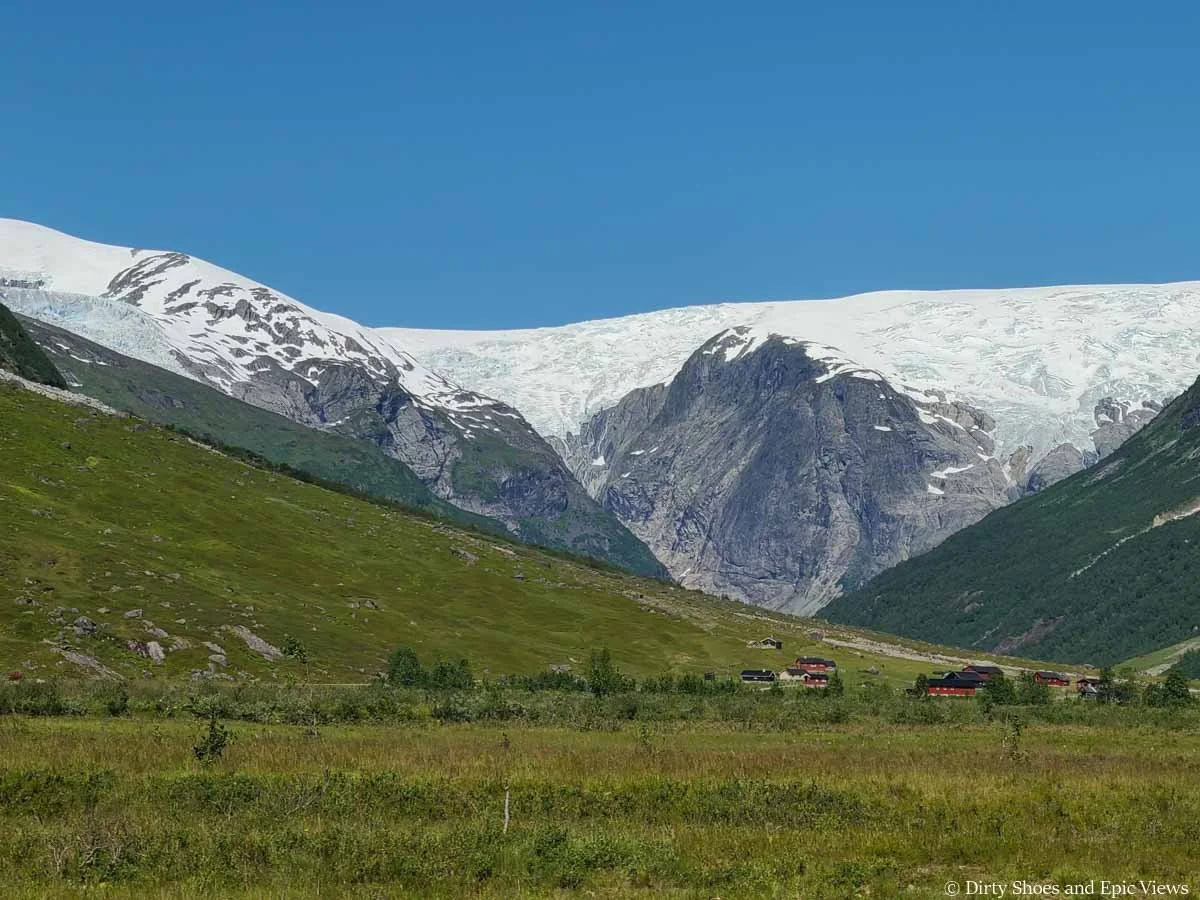 A ice cap sits on a mountain above a grassy valley as seen from the Austerdalsbreen toll road