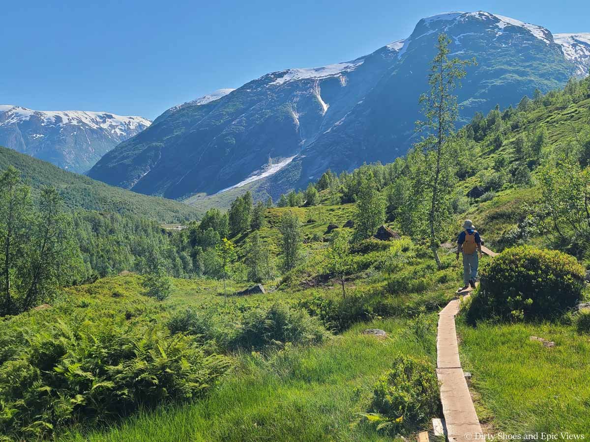 A hiker walks across a narrow boardwalk towards mountain views on the Austerdalsbreen hike