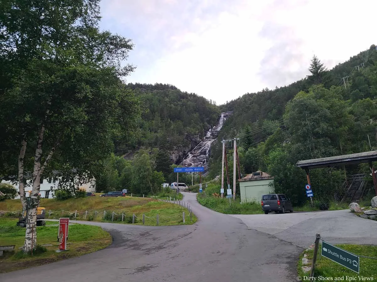 A narrow paved road leads to a blue banner that marks the P3 shuttle stop for Trolltunga