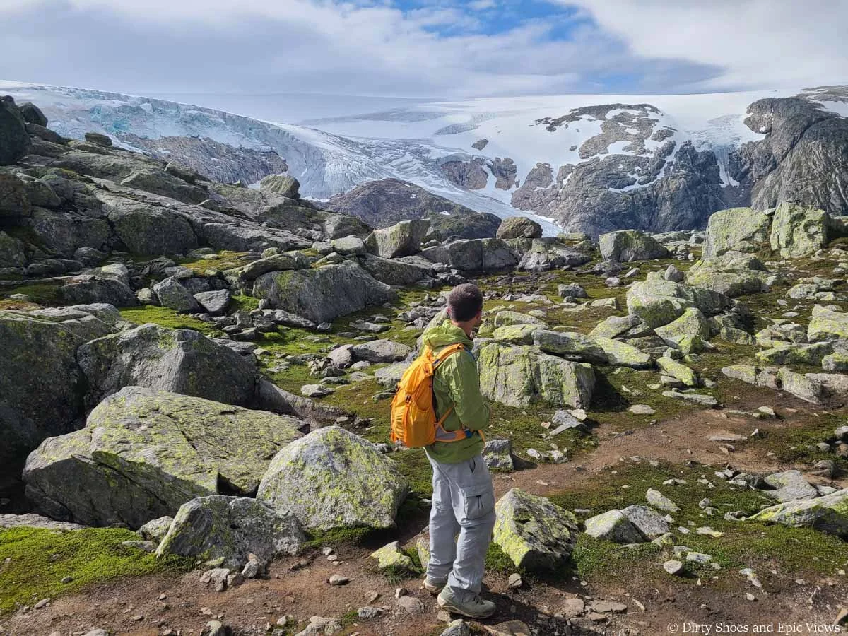 A hiker stands in a rocky meadow admiring views of a distant ice cap from the Reinanuten trail in Norway