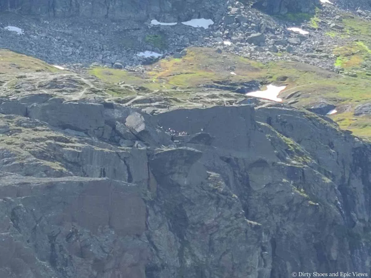 A zoomed in picture of Trolltunga from a far with barely visible people standing on the cliffs