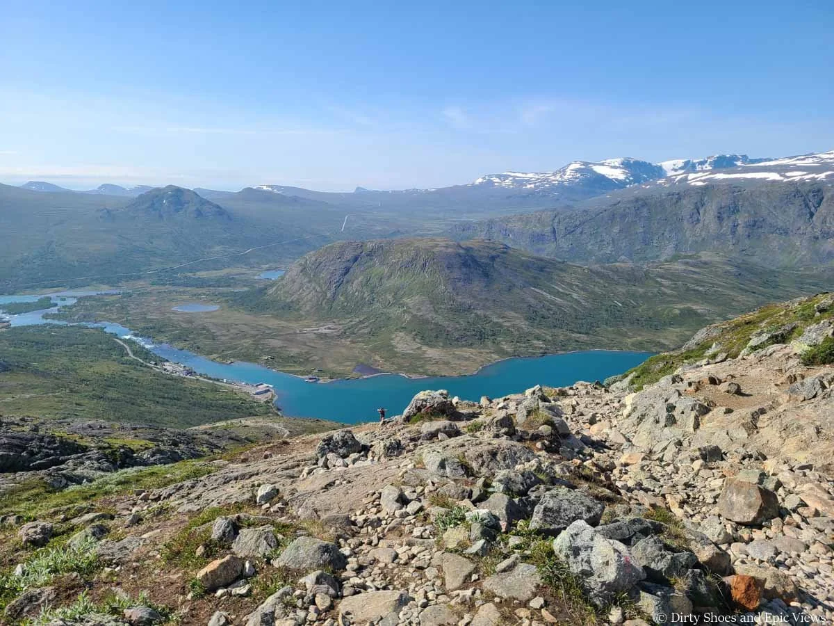 Looking down a rocky trail towards a lake surrounded by small mountains from the Besseggen Ridge trail in Norway