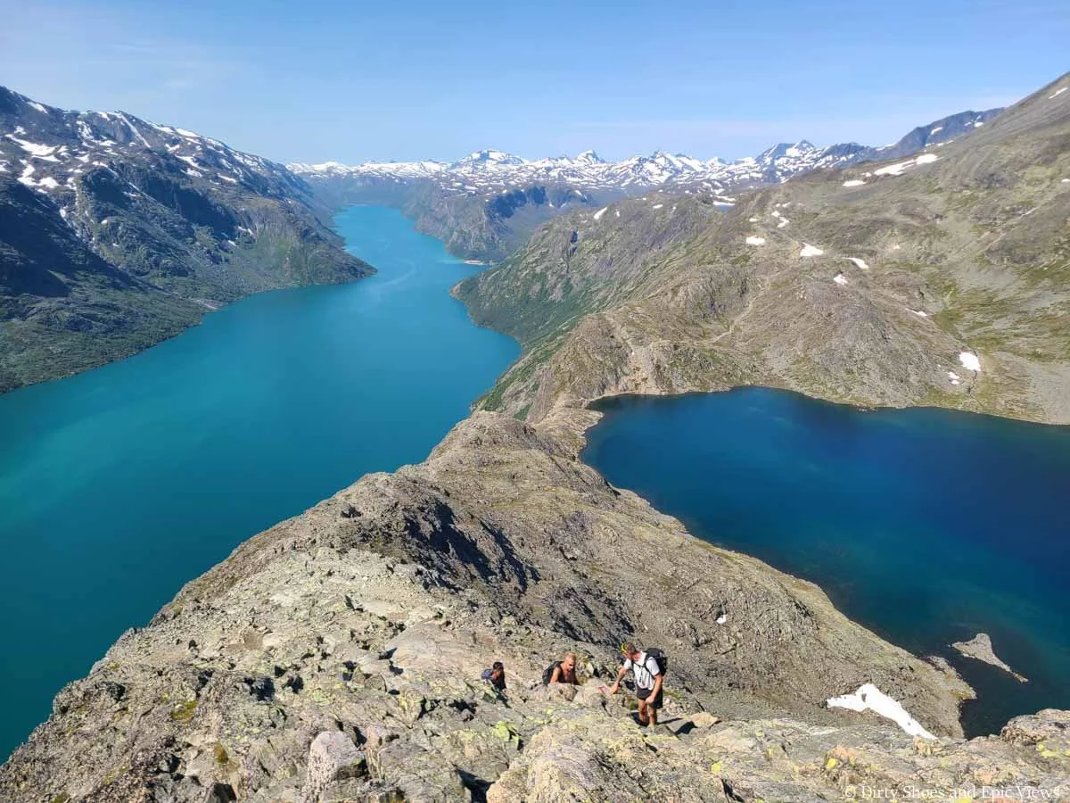 Three hikers ascend a rocky steep ridge between two blue lakes on the Besseggen Ridge trail in Norway