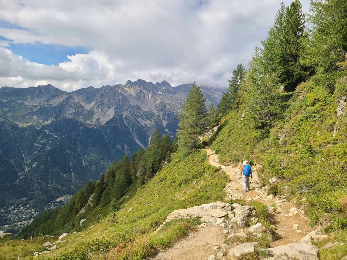 A hiker walks a dirt path along a grassy slope on the Grand Balcon Nord trail in Chamonix