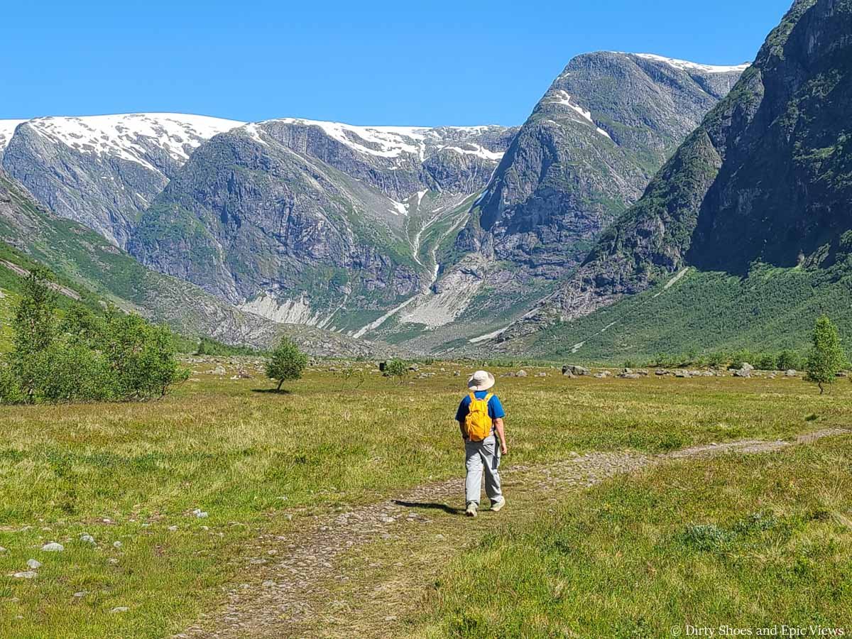 A hiker walks across a grassy meadow with mountain views on the Austerdalsbreen trail in Norway