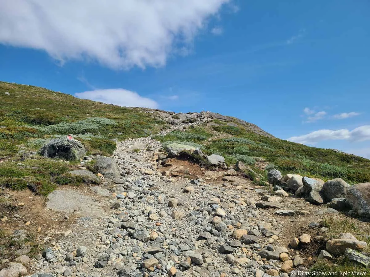 A steep path of loose rock climbs a grassy hill on Besseggen Ridge
