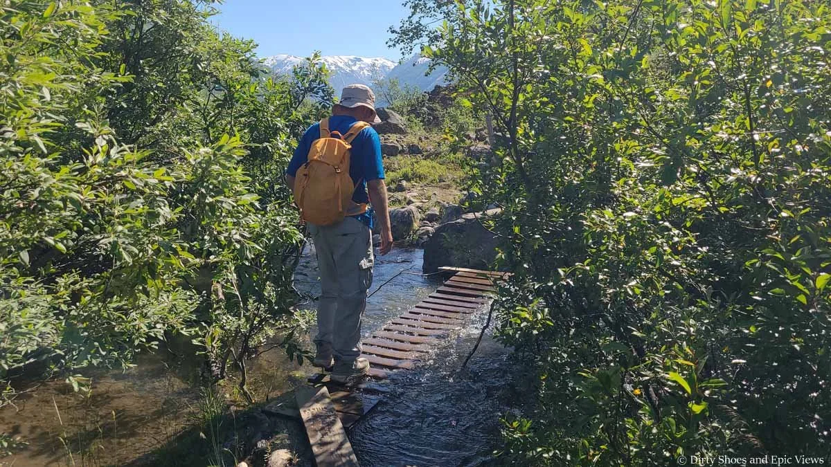 A hiker crosses a submerged footbridge through a stream on the Austerdalsbreen trail in Norway