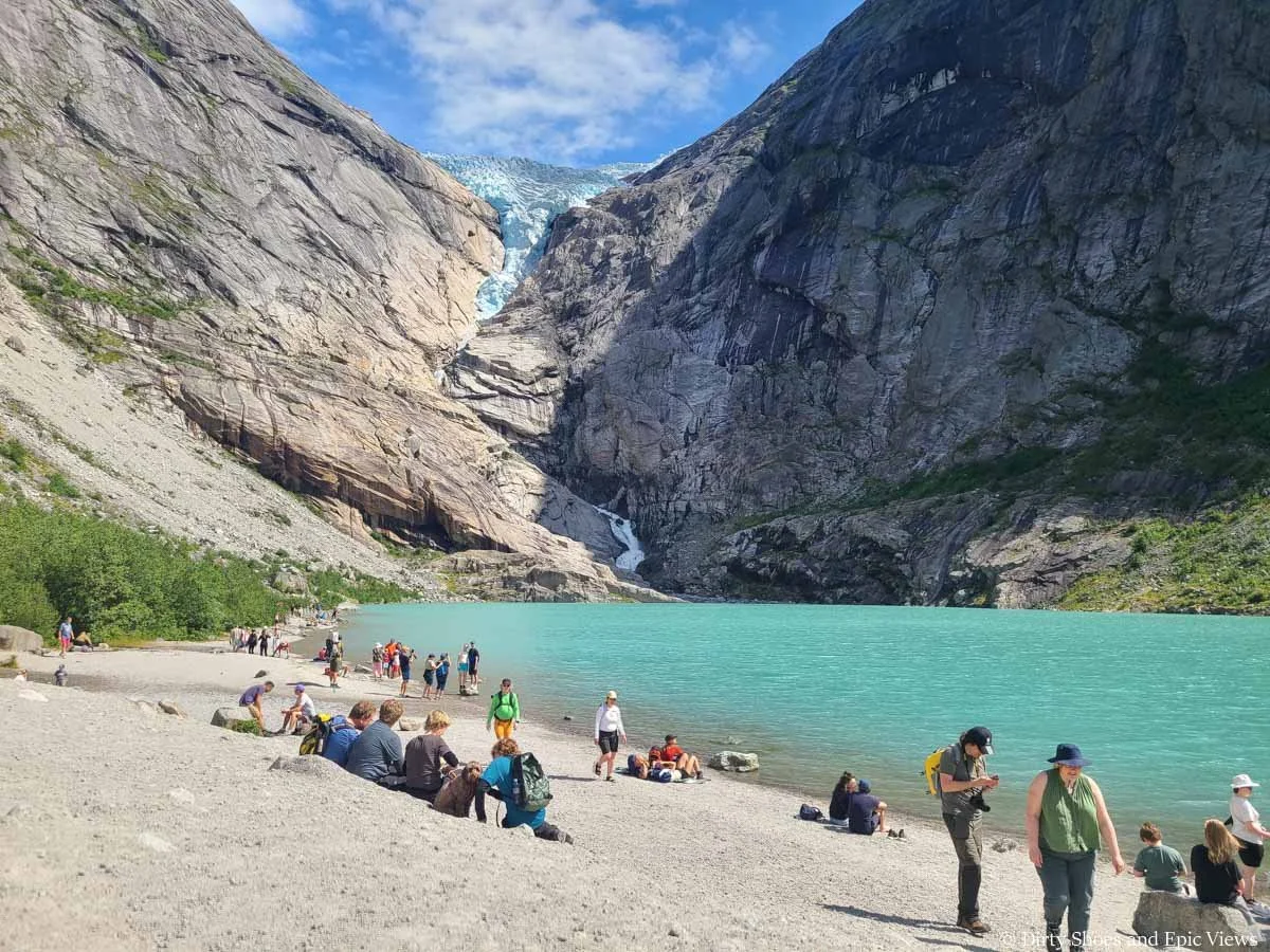 Crowds line the shore of a blue lake beneath a glacier at Briksdalsbreen in Norway