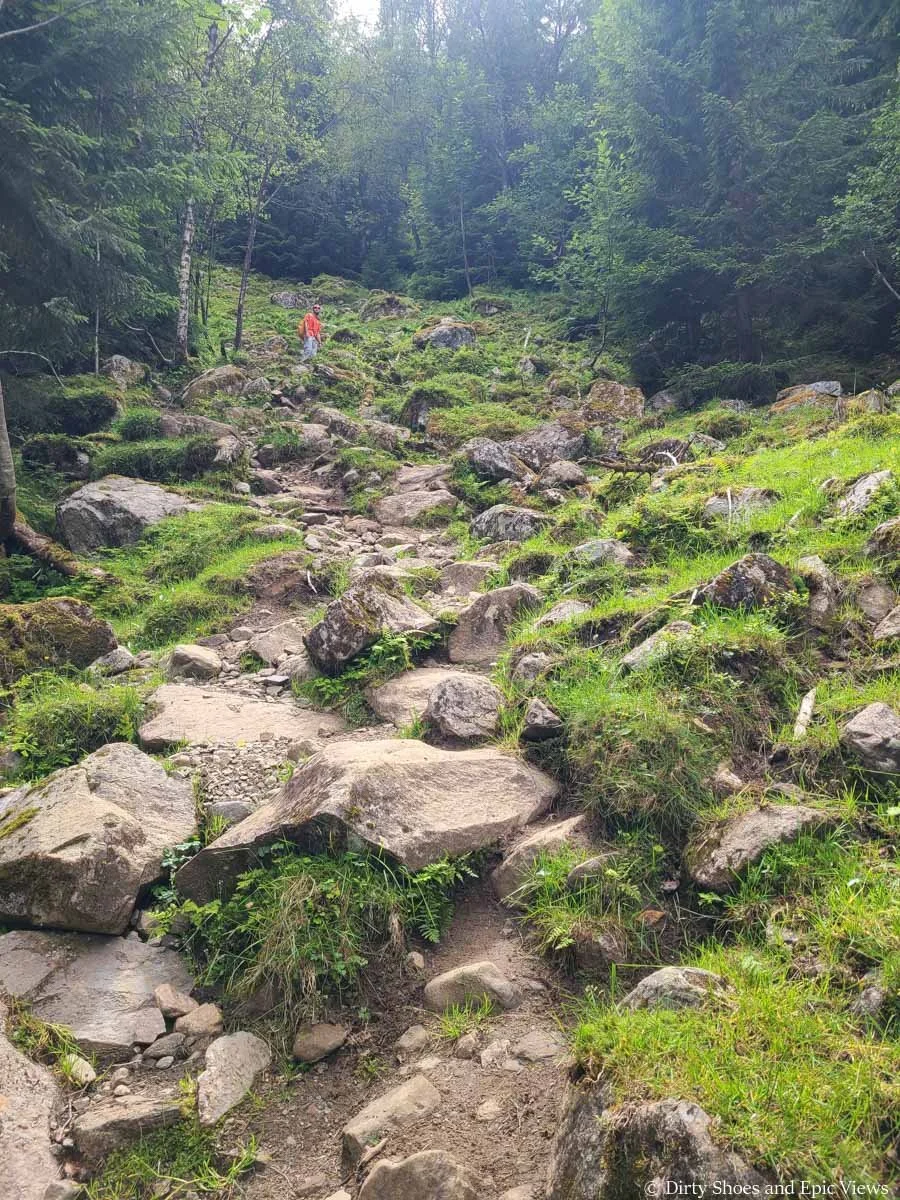 A hiker ascends a steep rocky trail to the Reinanuten viewpoint in Norway
