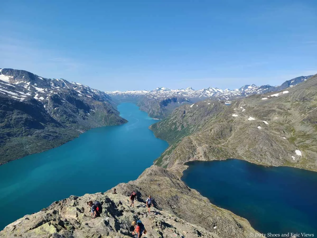 Hikers scramble up a narrow rock ridge between two blue lakes on the Besseggen Ridge trail in Norway