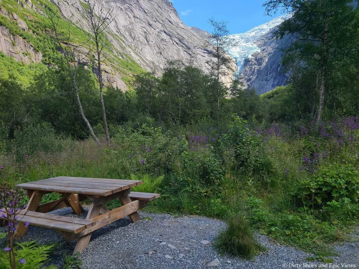 A picnic table sits in the brush with scenic views to a glacier along the Briksdalsbreen hike in Norway