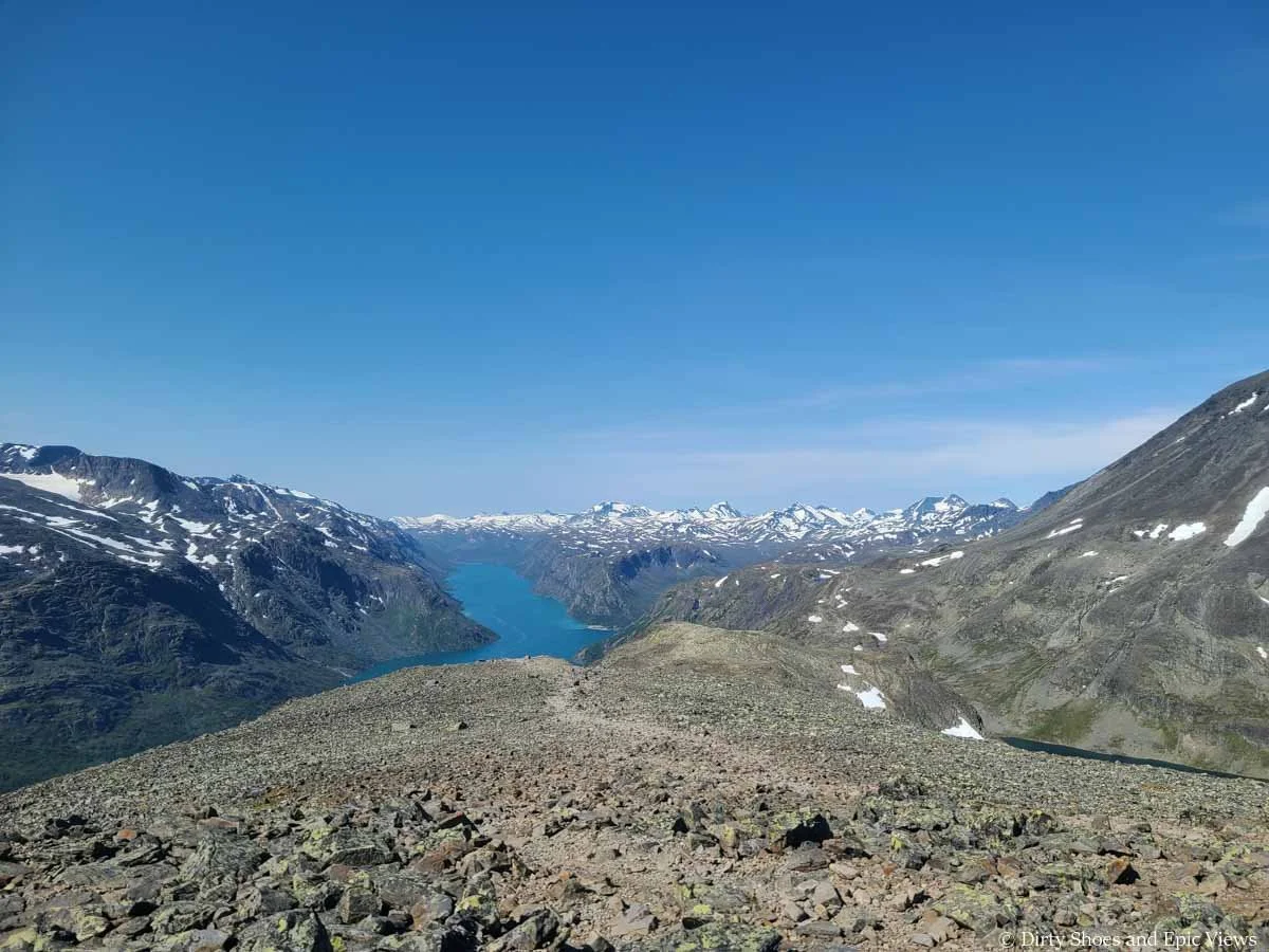 A faint herd path descends gradually down a rocky landscape towards a lake on the Besseggen Ridge trail in Norway