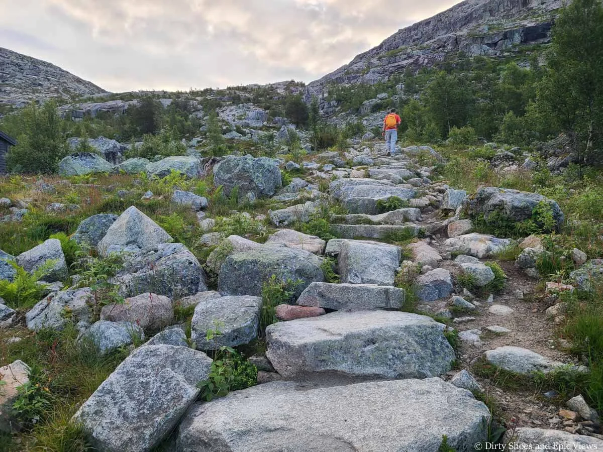 A hiker ascends a steep stone staircase up a mountain pass on the Trolltunga hike