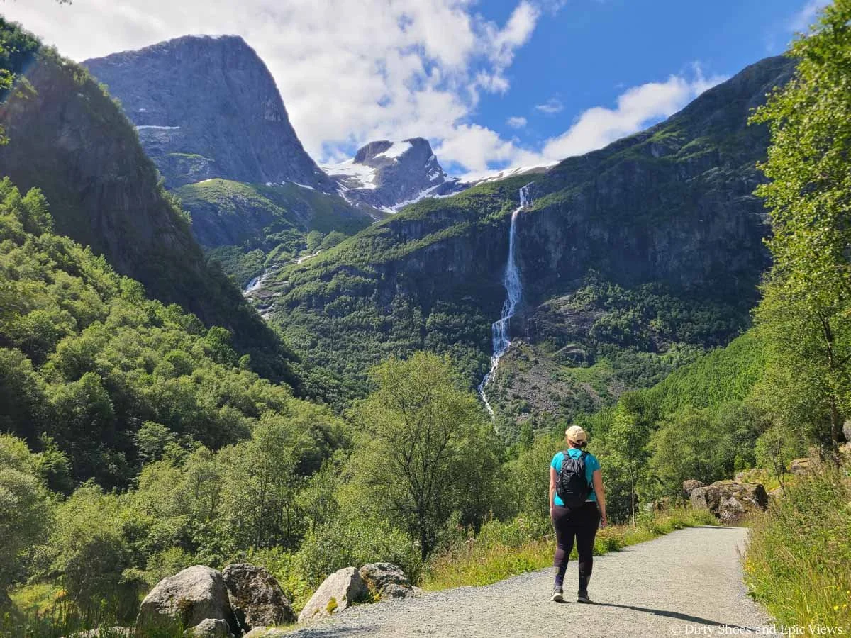 A hiker walks a path towards mountain and waterfall views on the Briksdal Glacier hike in Norway