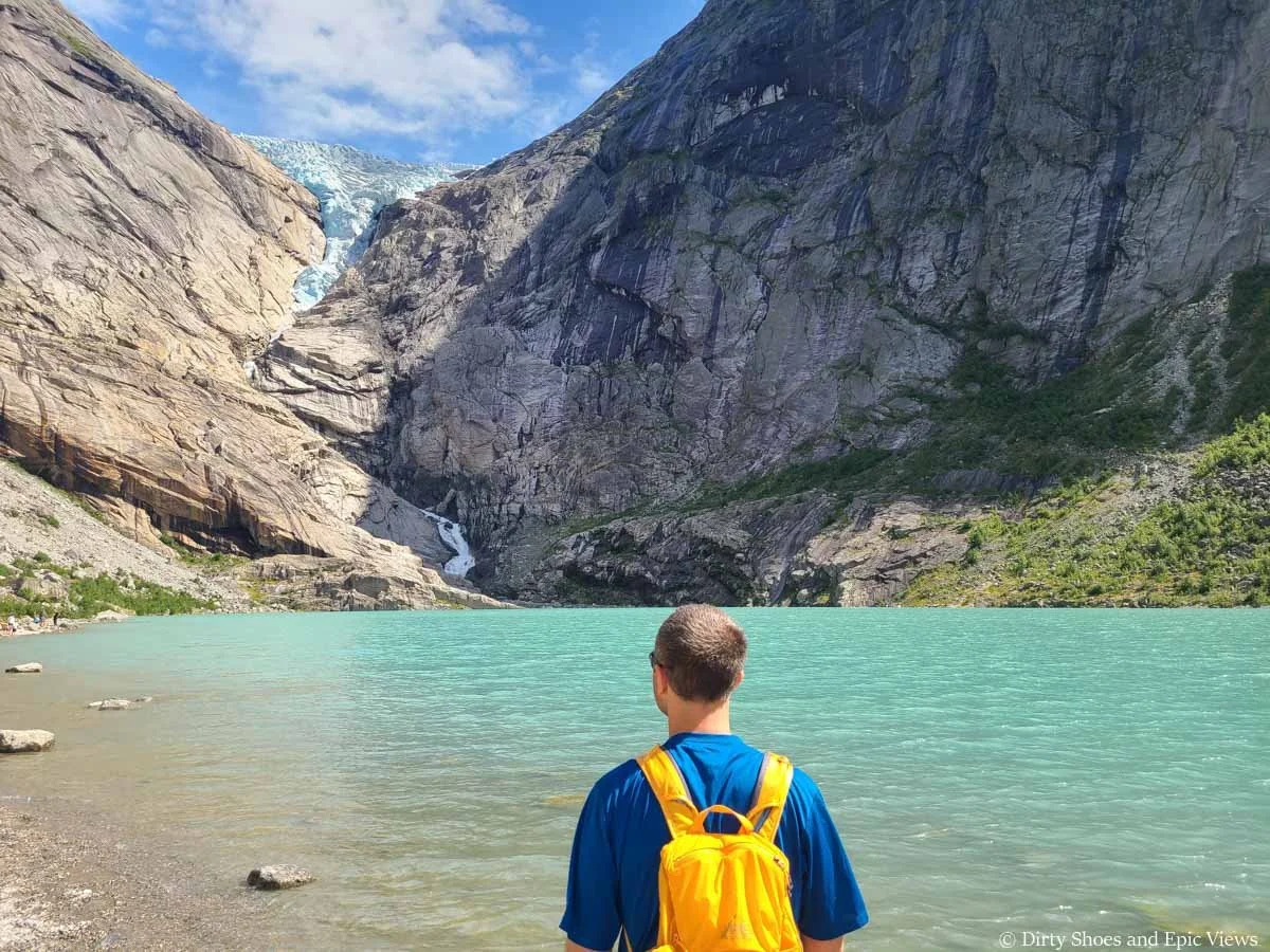 A hiker looks out over a blue lake to a glacier at Briksdalsbreen in Norway