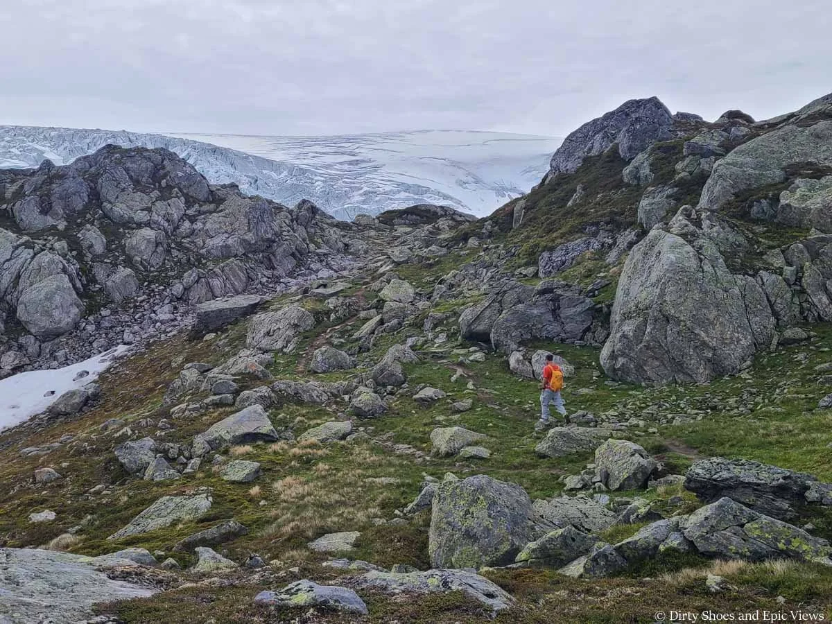 A hiker walks through a rocky meadow towards views of an ice cap along the Reinanuten hike in Norway