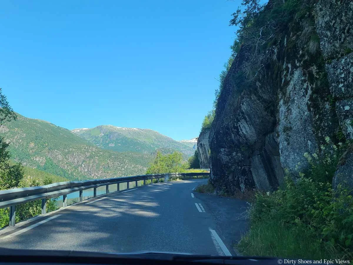 A narrow road makes a blind turn around a rock wall on the drive to Austerdalsbreen