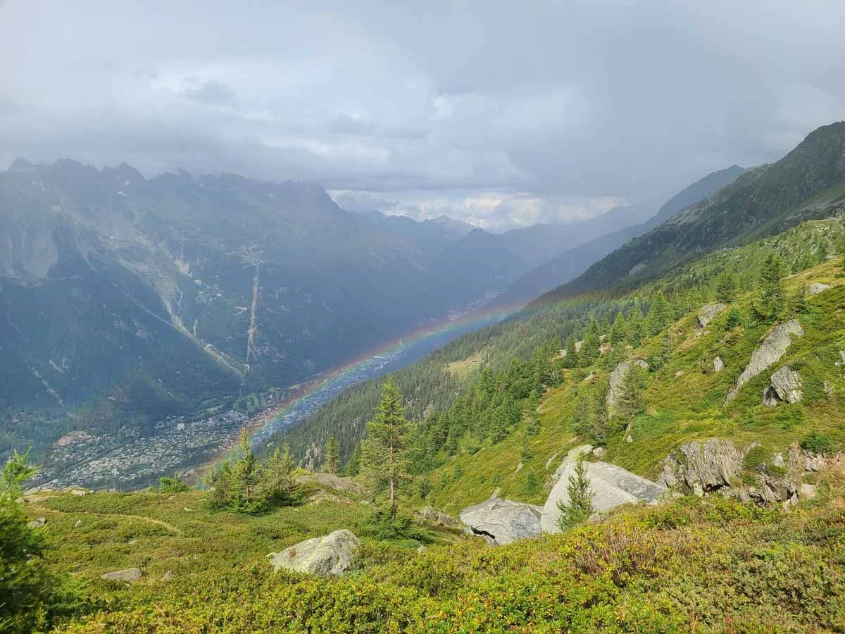 A rainbow stretches above a subalpine meadow and a valley below on the Grand Balcon Nord trail in Chamonix