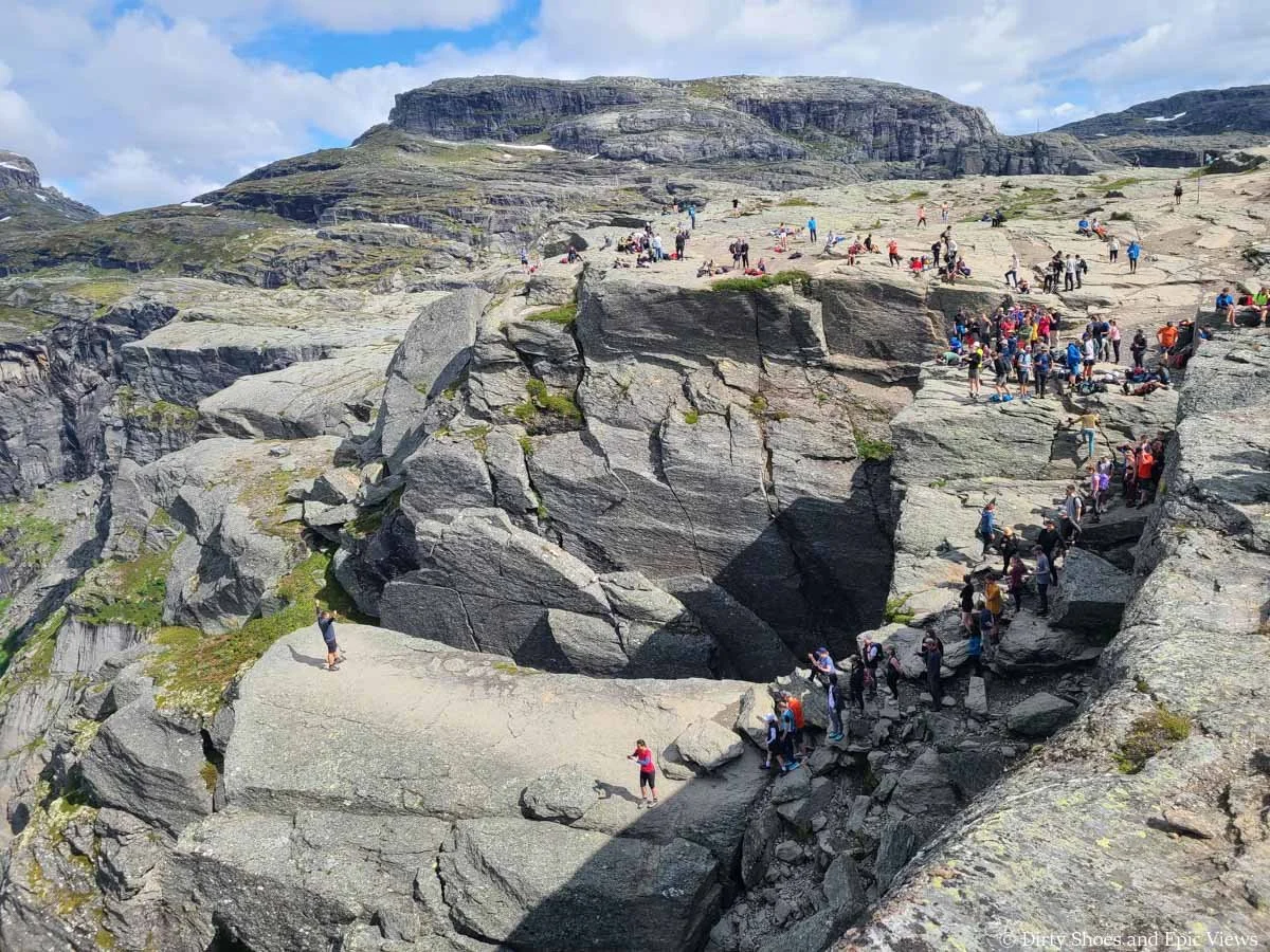 A line of people stands on a rocky cliff edge waiting to pose on Trolltunga