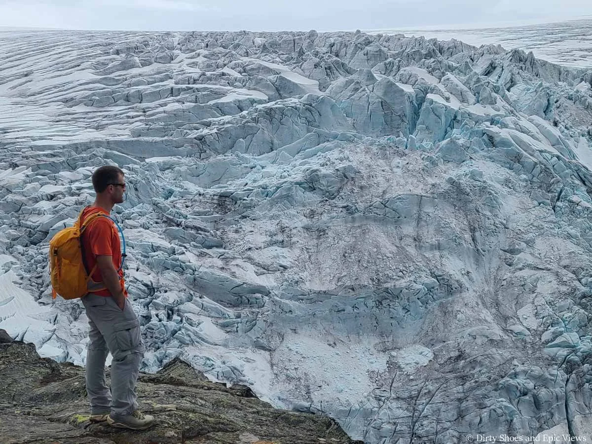 A hiker stands in front of views of a massive ice cap where its crevasses and features can be seen up close from the Reinanuten trail in Norway