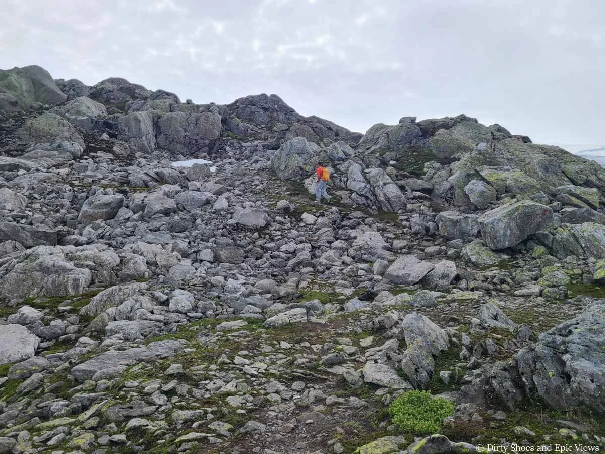 A hiker ascends a large rocky hill along the Reinanuten hike in Norway