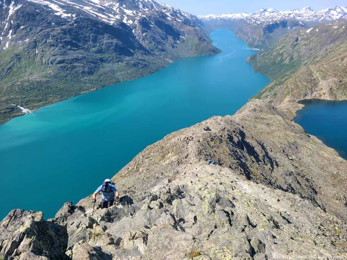 A path leads down a narrow rocky spine between two blue lakes on the Besseggen Ridge trail in Norway