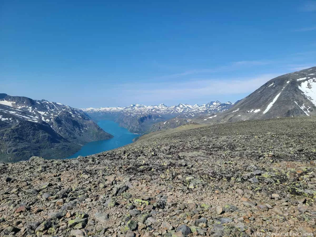 Snow covered mountains surround a turquoise lake as seen from Besseggen Ridge in Norway