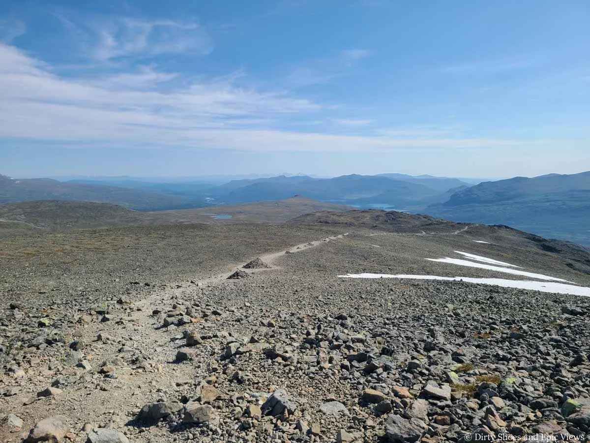 A faint herd path through a rocky landscape is marked by large rock cairns along the Besseggen Ridge trail in Norway