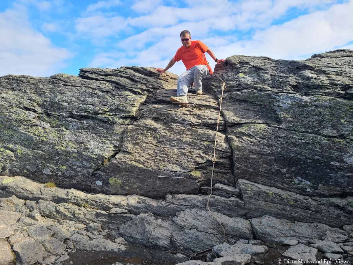 A hiker climbs down metal rungs down a rock face using a rope for support at Trolltunga in Norway