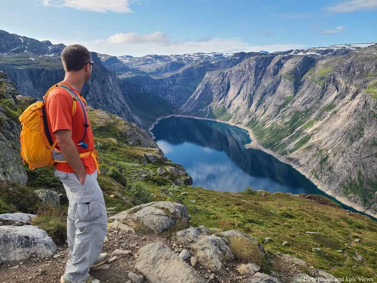 A hiker looks out over a deep blue lake surrounded by steep cliffs along the Trolltunga trail