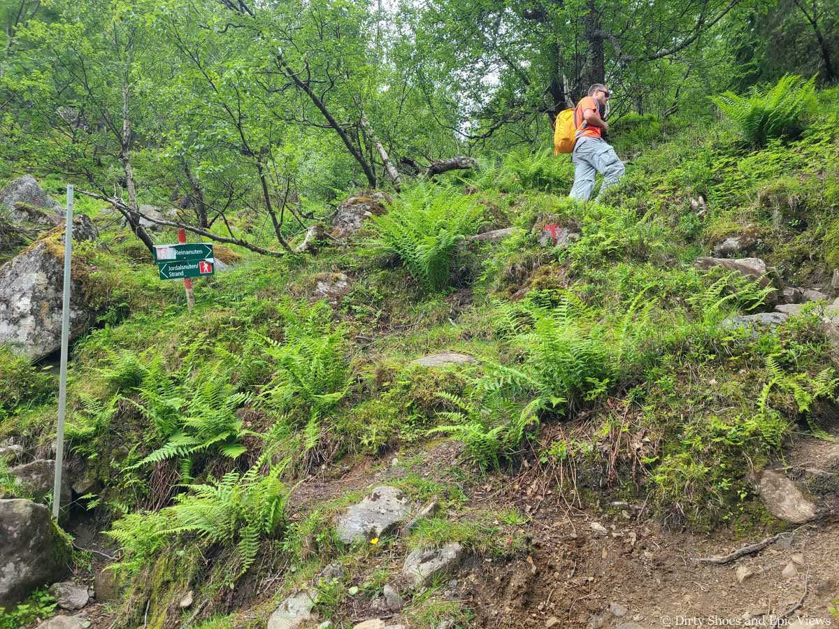 A hiker ascends a steep trail past a junction on the Reinanuten hike in Norway