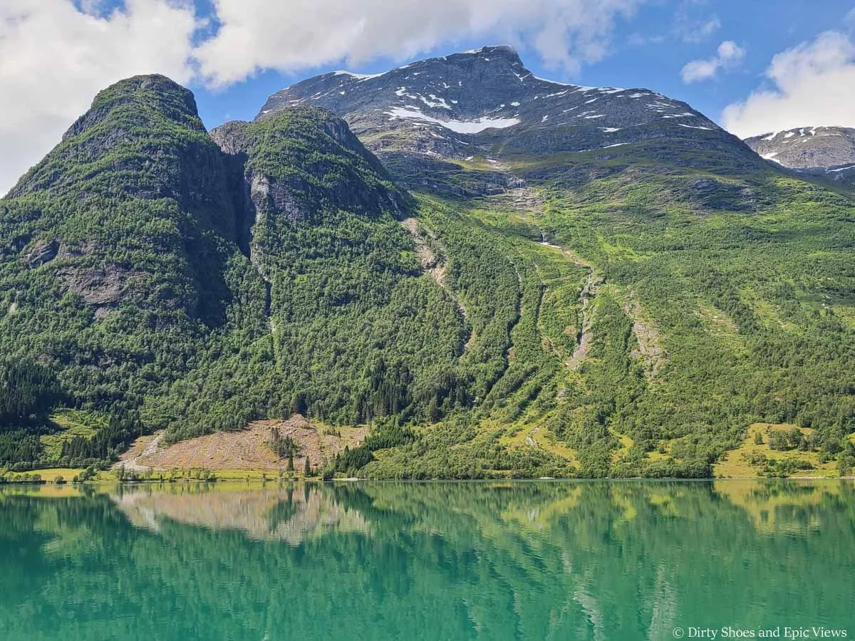 A reflective blue lake sits beneath green mountains on the drive to the Briksdal Glacier in Norway