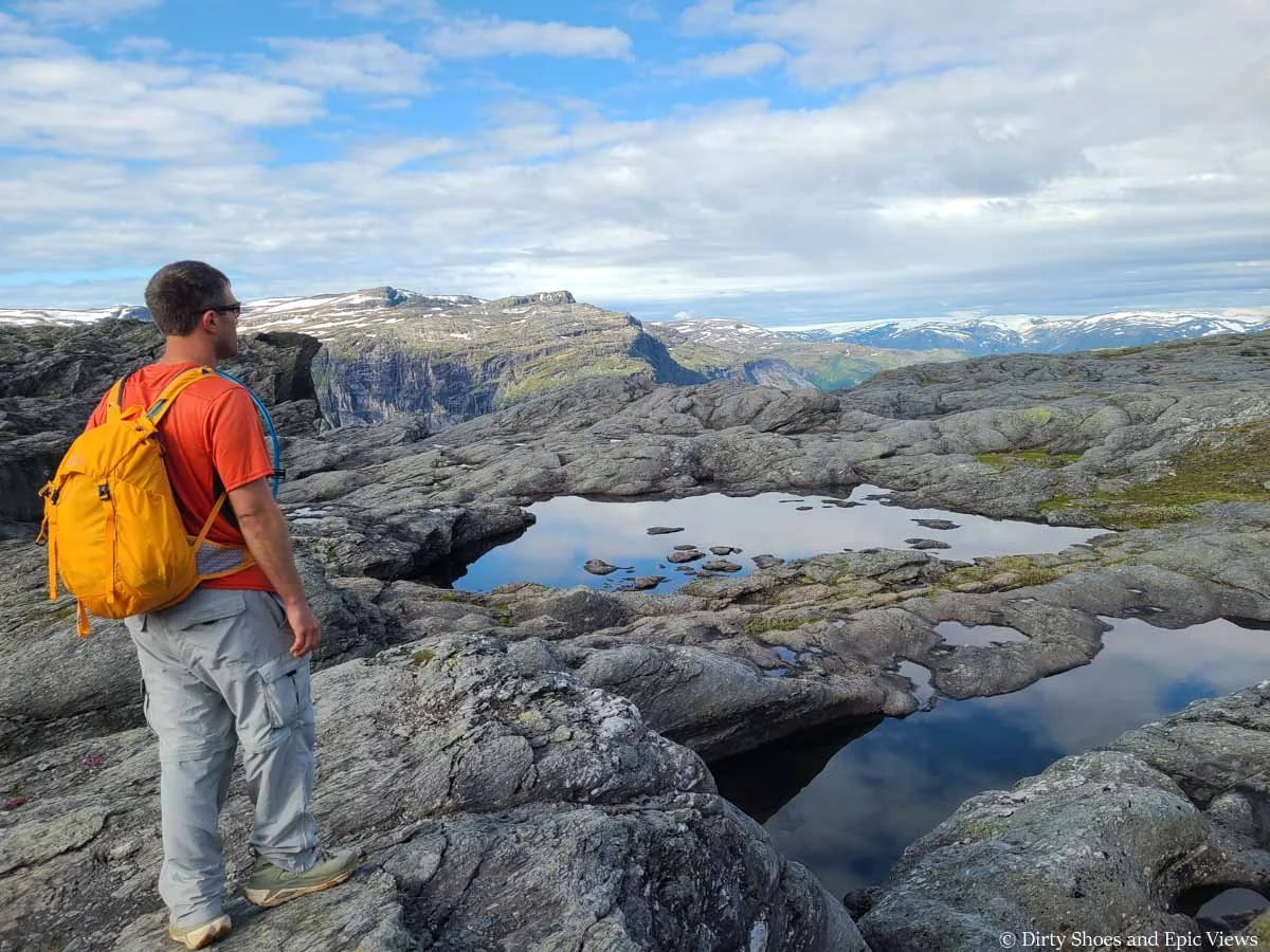 A hiker looks out over a rocky landscape and small still tarns along the Trolltunga hike in Norway