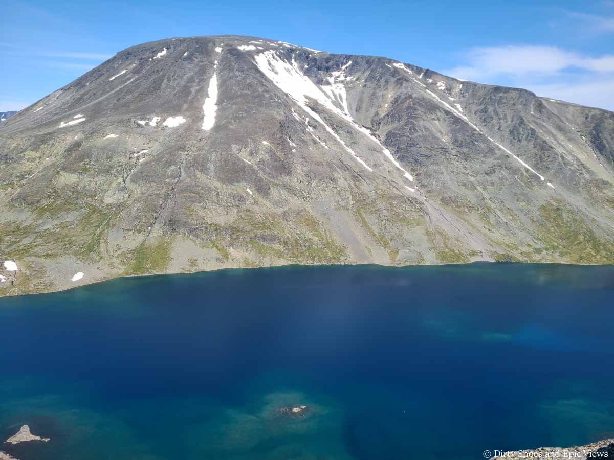 A large mountain towers over a deep blue lake along the Besseggen Ridge trail in Norway