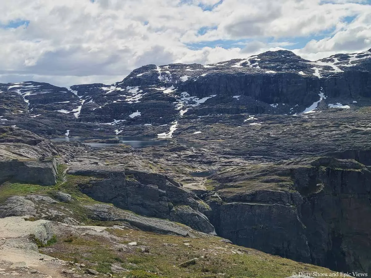 A rocky landscape with small tarns sits beneath snowy cliffs along the Trolltunga trail in Norway