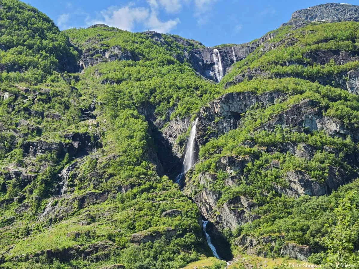 A multi-tiered waterfall runs down a lush cliffside on the drive to Briksdalsbreen in Norway