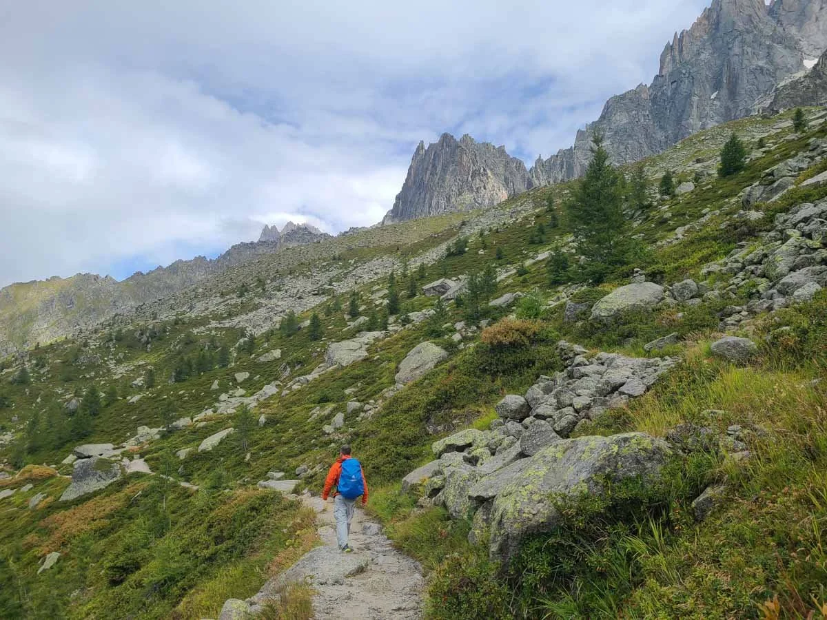 A hiker walks a dirt path along the slopes of Chamonix mountains on the Grand Balcon Nord