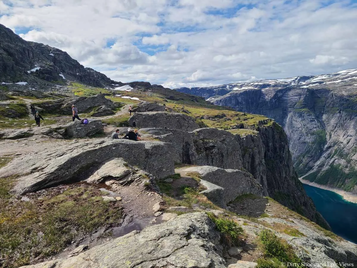 People scatter across a rocky clifftop overlooking a blue lake near Trolltunga in Norway