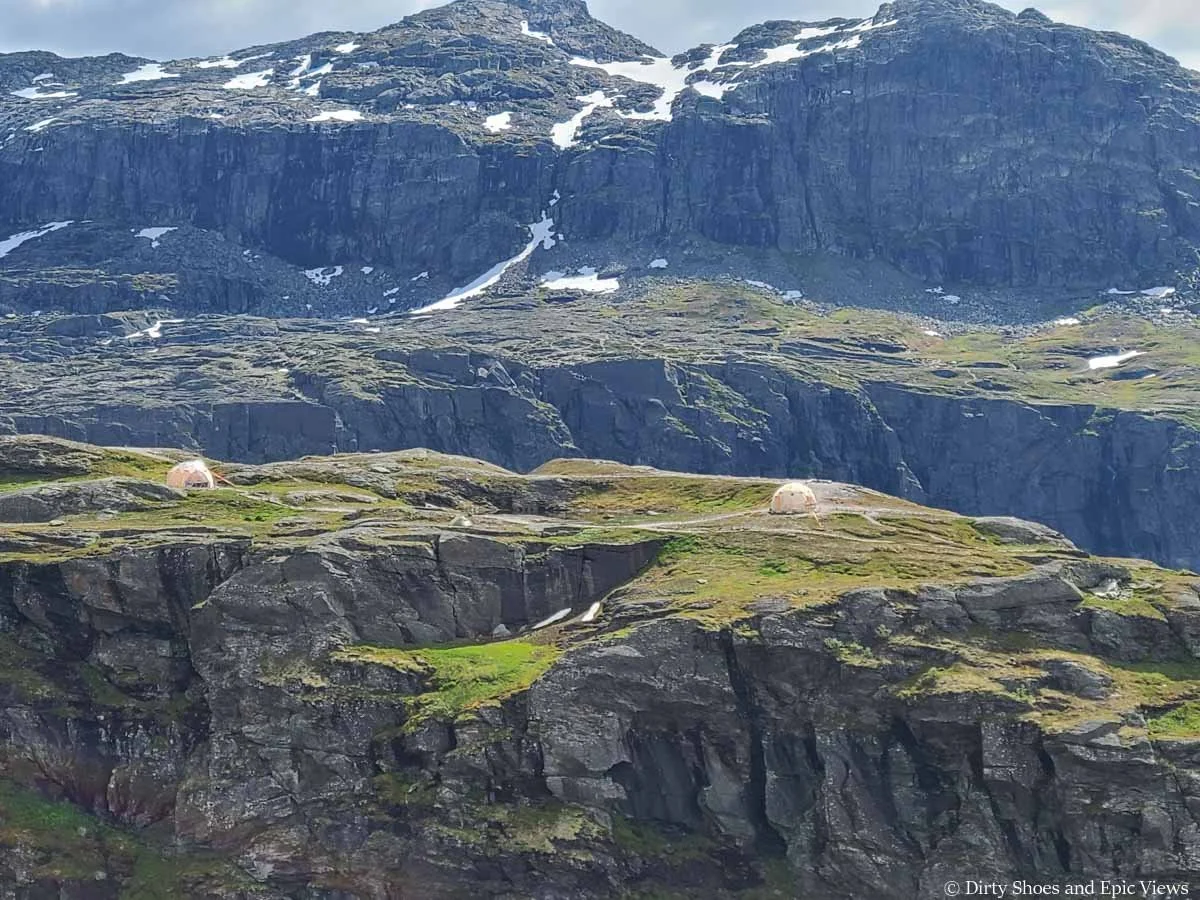 Tents sit on a grassy cliff top with steep rocky cliffs behind them near Trolltunga